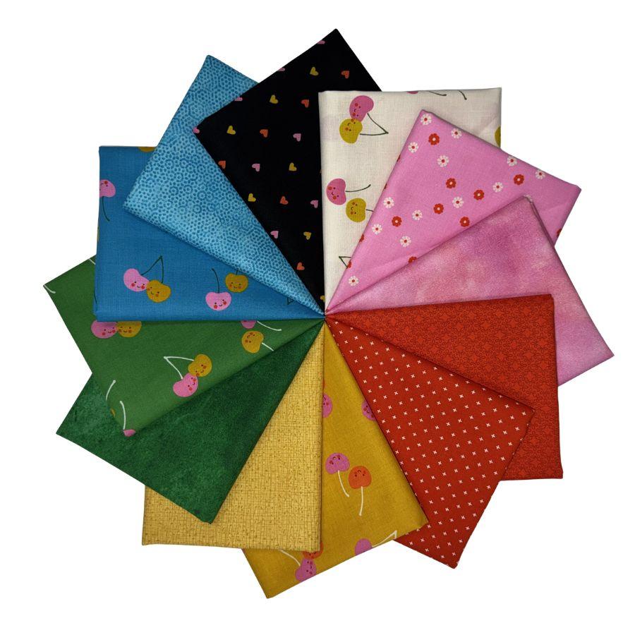 A fan arrangement of multiple fabric squares in different colors and patterns, including blue, black, cream, pink, red, yellow, and green, each with cherry or polka-dot motifs, on a white background.